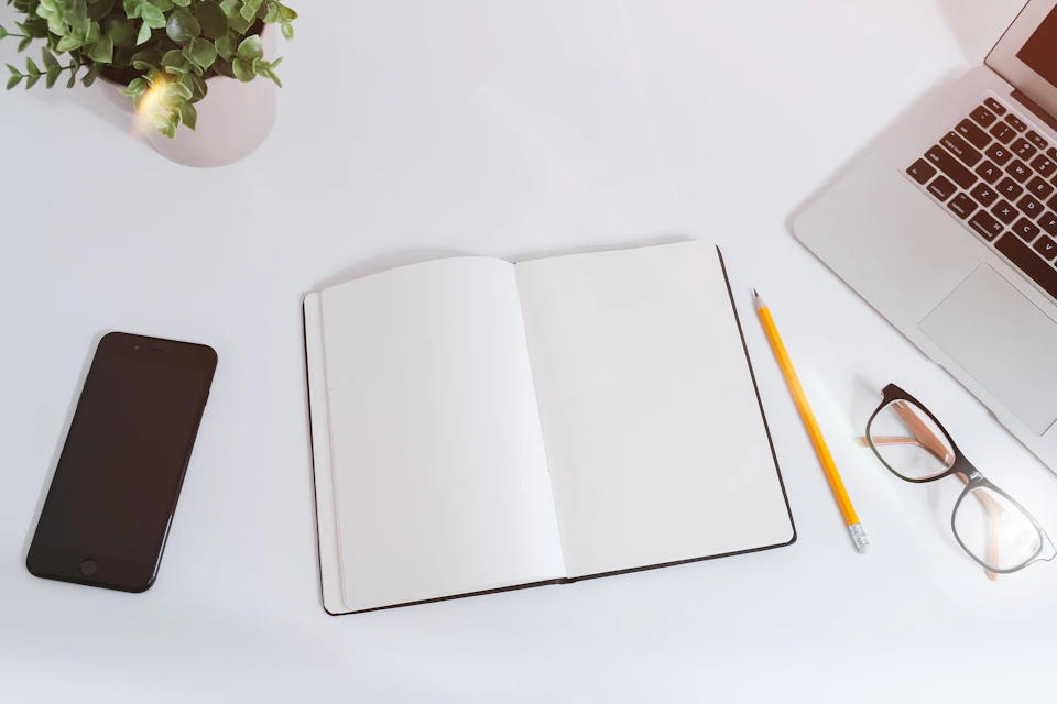 Open notebook and pencil beside a laptop on a white desk. Conceptual stock photograph.