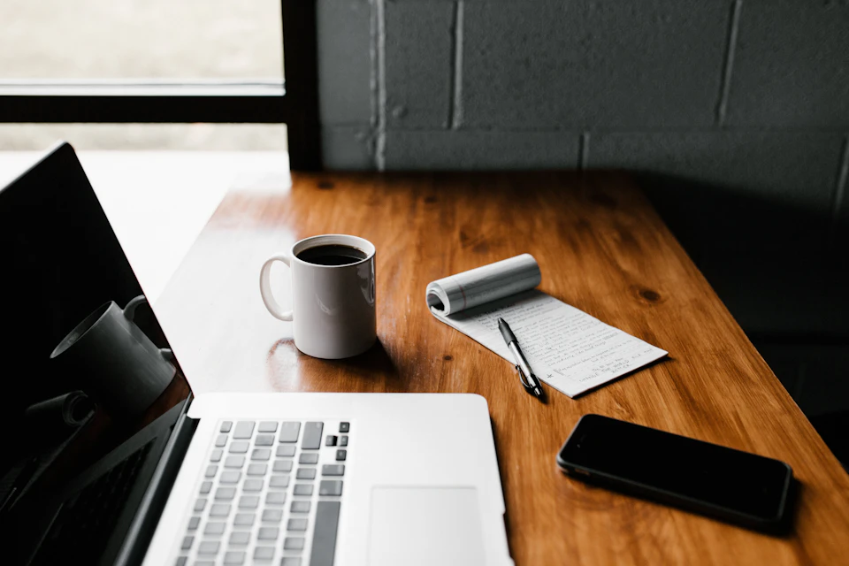 Laptop, notebook and coffee arranged on a wooden desk. Conceptual stock photograph.